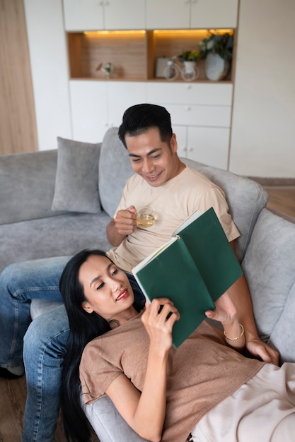 Foto grátis casal carinhoso em casa no sofá lendo livro e tomando uma bebida