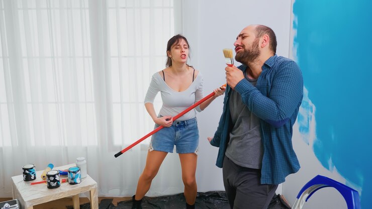 Foto grátis casal casado cantando em ferramentas de renovação mergulhadas em tinta azul. casal alegre durante a reforma em casa. decoração de casa e reforma em apartamento aconchegante, reforma e reforma