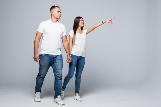 Casal casual caminhando em direção à câmera, olhando um para o outro, isolado na parede branca