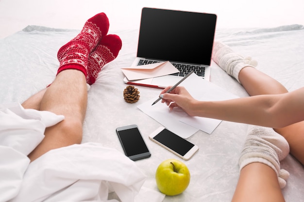 Casal caucasiano em casa usando tecnologia de internet. Laptop e telefone para pessoas sentadas no chão em meias coloridas. Natal, amor, conceito de estilo de vida