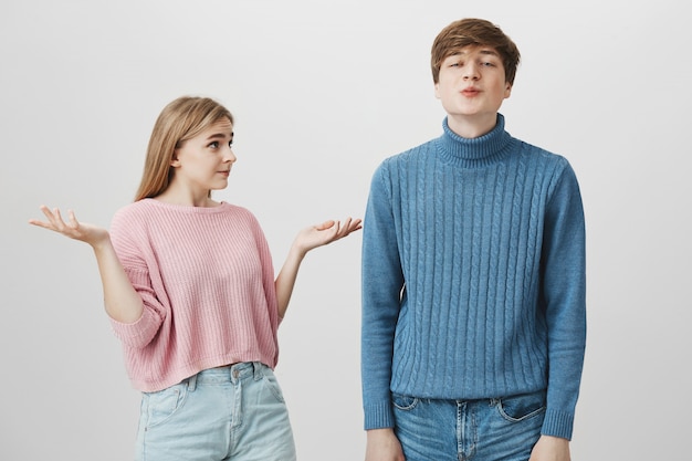 Casal caucasiano emocional. Jovem macho vestido de suéter azul faz beicinho, manda beijos