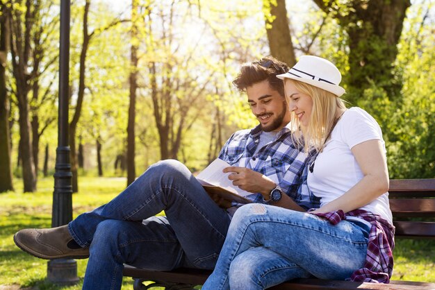 Casal caucasiano feliz sentado em um banco de parque, lendo um livro juntos