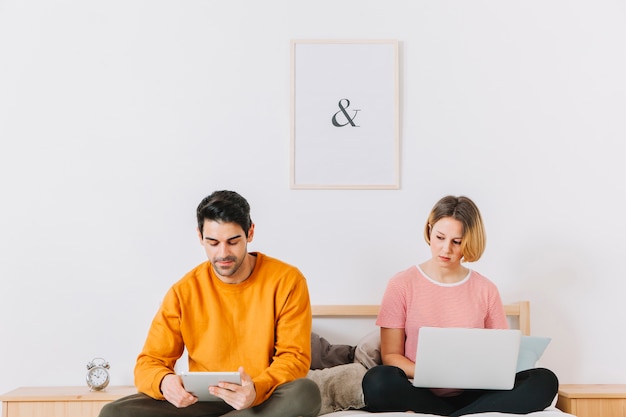 Casal com laptop e tablet no quarto