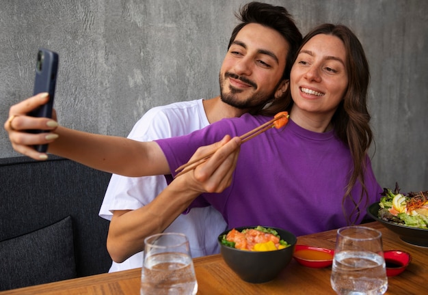 Foto grátis casal comendo tigela de prato de salmão no restaurante e tirando selfie