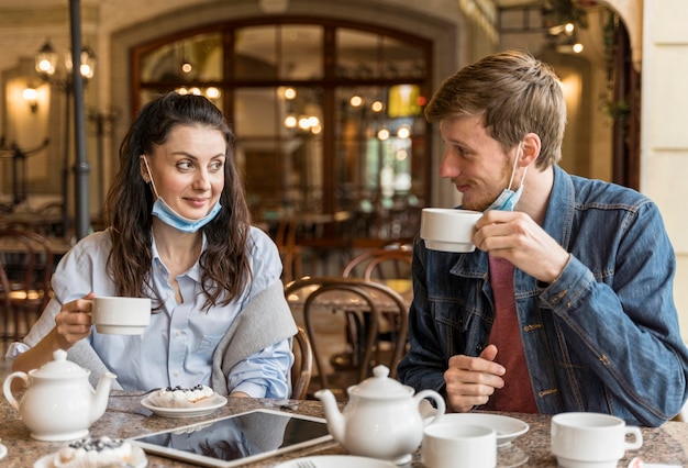 Casal conversando no restaurante com máscaras médicas no queixo