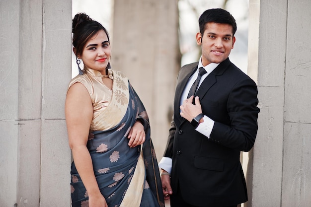 Casal de amigos indianos elegantes e elegantes de mulher em saree e homem de terno posado sob arco