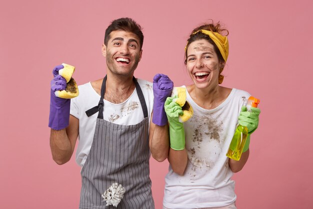 Casal de família feliz e alegre cerrando os punhos com entusiasmo, sendo feliz em limpar todos os quartos de sua casa, regozijando seus resultados. Trabalhadores bem-sucedidos do sexo masculino e feminino do serviço de limpeza