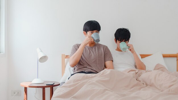 Casal de gays asiáticos falando divertindo-se em casa moderna. Jovem amante da Ásia LGBTQ + masculino feliz relaxar descansar beber café depois de acordar enquanto estava deitado na cama no quarto em casa de manhã.