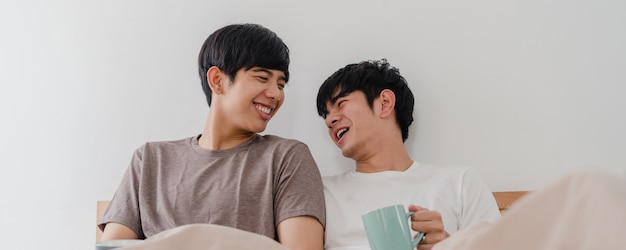 Casal de gays asiáticos falando divertindo-se em casa moderna. Jovem amante Ásia masculino feliz relaxar resto beber café depois de acordar enquanto estava deitado na cama no quarto em casa de manhã.