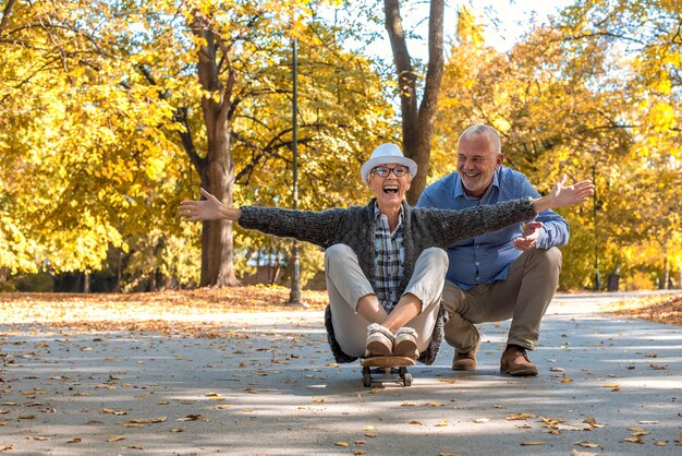 Casal de idosos com uma mulher sentada no skate no parque