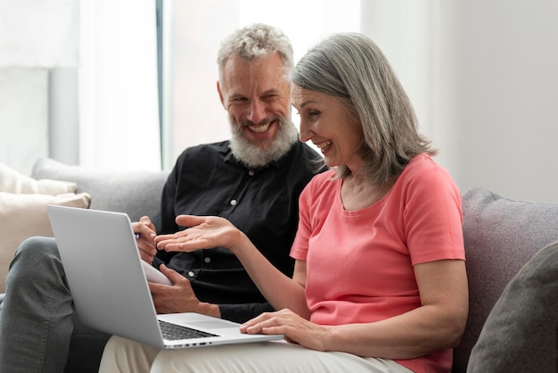 Casal de idosos em casa no sofá usando laptop