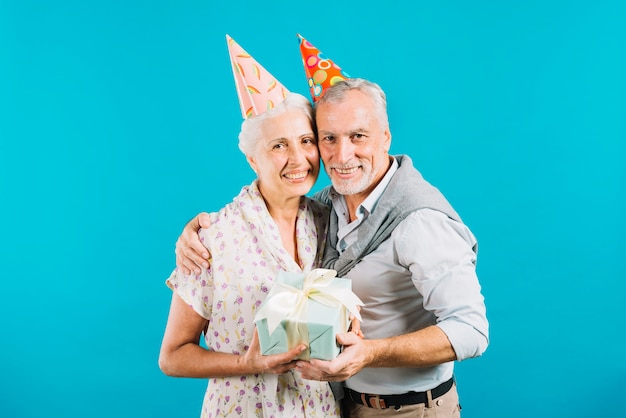 Casal de idosos feliz segurando o presente de aniversário em fundo azul