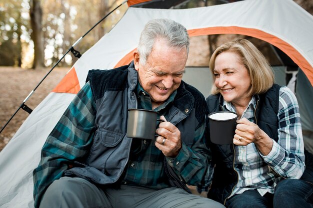 Casal de idosos felizes tomando café perto da barraca na floresta