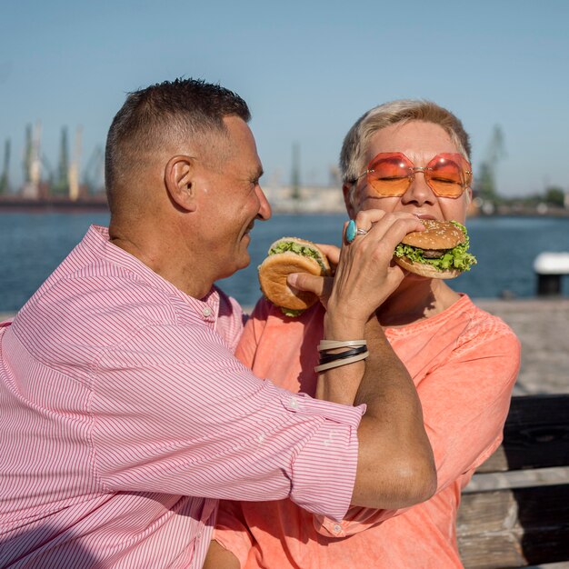 Casal de idosos na praia comendo hambúrgueres