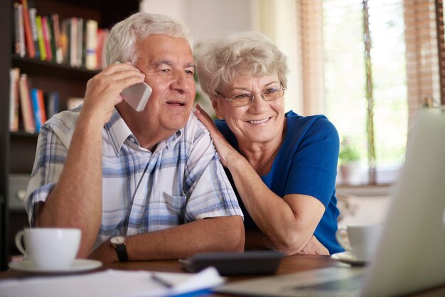 Casal de idosos sorrindo fazendo negócio por telefone