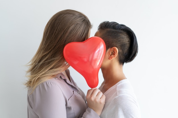 Casal de lésbicas beijando atrás de balão em forma de coração