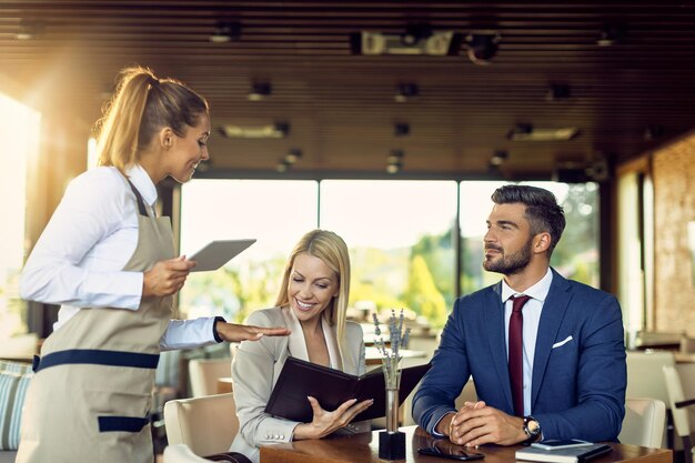 Casal de negócios conversando com garçonete enquanto escolhe o pedido de um menu em um restaurante