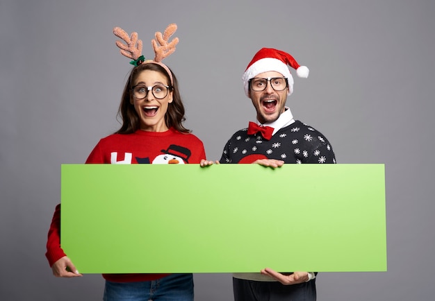 Casal de nerds segurando banner de Natal em tela verde com espaço de cópia