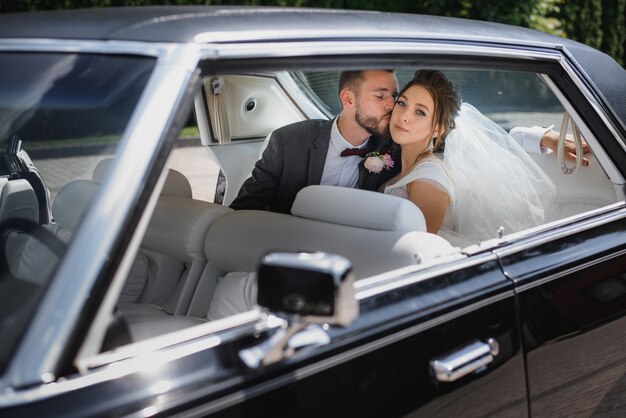 Casal de noivos estão sentados no banco de trás de um carro e beijando