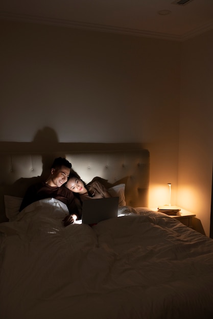 Casal de tiro médio assistindo filme na cama