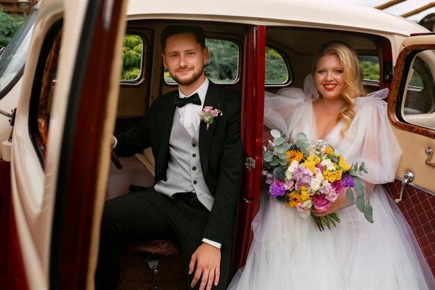 Casal de tiro médio posando em carros antigos