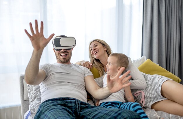 Casal deitado com o filho e assistindo a algo com o fone de ouvido de realidade virtual