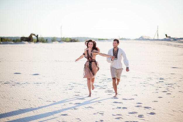 Casal descalço em roupas bordadas brilhante corre em uma areia branca