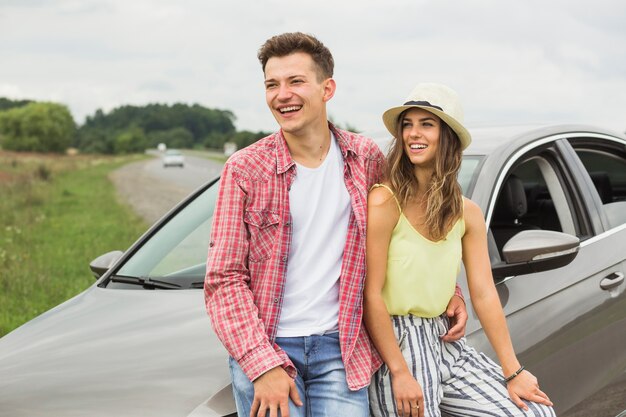 Casal elegante feliz sentado sobre o capô do carro