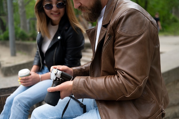 Casal em jaquetas de couro sintético usando câmera fotográfica ao ar livre