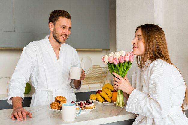 Casal em roupões de banho na cozinha com buquê de tulipas