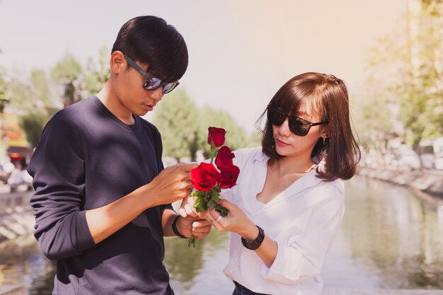 Casal em um parque com rosas nas mãos e óculos de sol