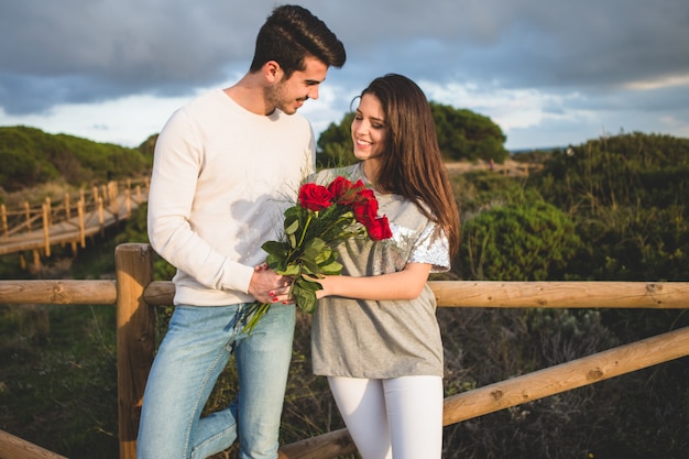 Foto grátis casal encostado em uma grade de uma ponte com um buquê de rosas