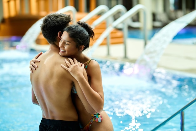 Casal feliz apaixonado abraçando enquanto se diverte na piscina do spa