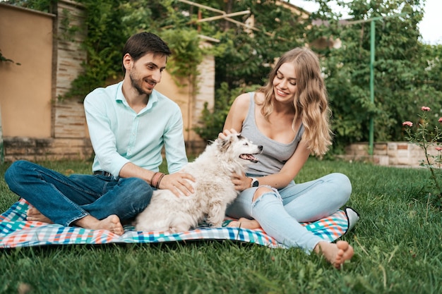 Casal feliz brincando com seu cachorro no quintal na grama. Cachorro velho alegre