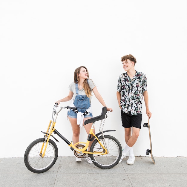 Casal feliz com bicicleta e skate olhando uns aos outros