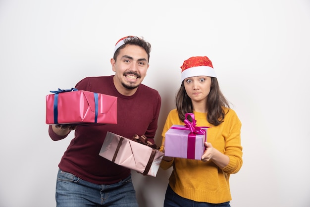 Casal feliz com presentes de Natal, por cima de uma parede branca.