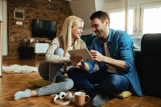 Casal feliz conversando e se divertindo enquanto navega na net em tablet digital na sala de estar