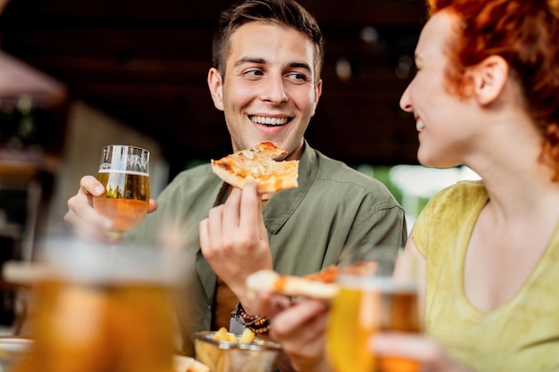 Casal feliz conversando enquanto come pizza e bebe cerveja em um pub