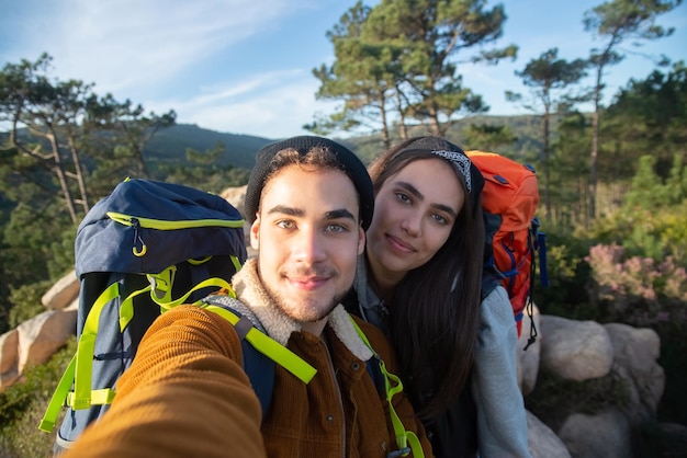 Casal feliz de caminhantes tomando selfie. Homem e mulher em roupas casuais e com mochilas, olhando para a câmera. Amor, lazer, conceito de tecnologia