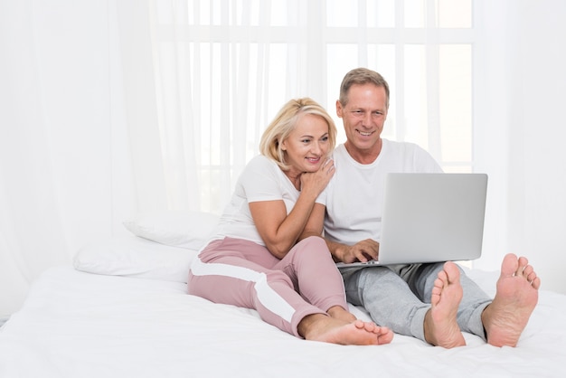 Casal feliz de tiro completo com laptop no quarto