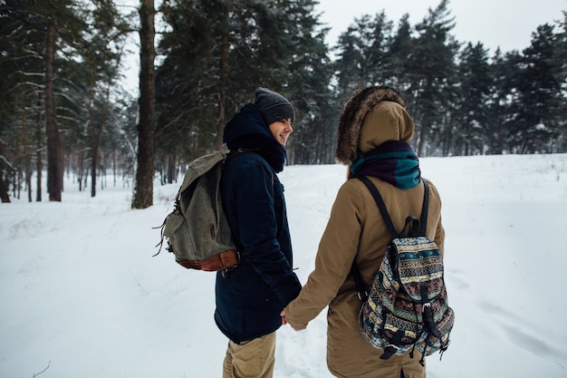 Casal feliz de viajantes de mãos dadas na floresta de inverno nevado