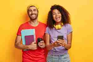 Foto grátis casal feliz e elegante posando contra a parede amarela com gadgets