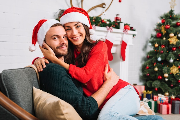 Casal feliz em chapéus de Natal abraçando no sofá