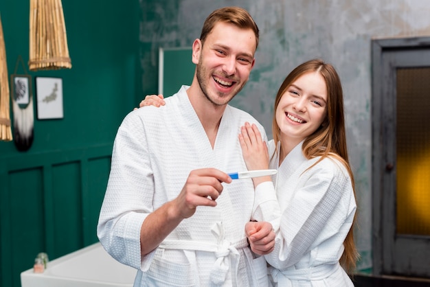 Casal feliz em roupões segurando o teste de gravidez