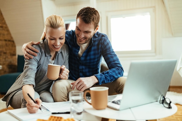 Casal feliz escrevendo notas enquanto passa pelas finanças domésticas durante a hora do café