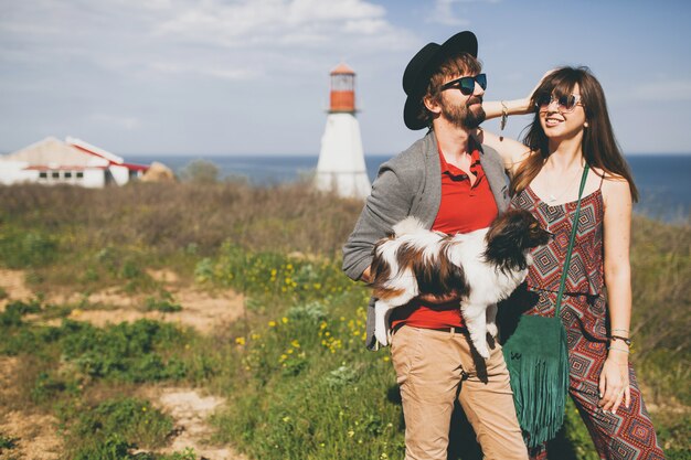 Foto grátis casal feliz, jovem e elegante hippie apaixonado, caminhando com um cachorro no campo