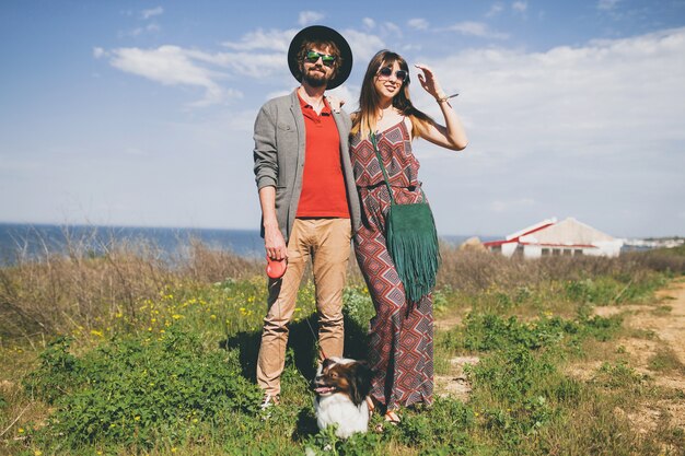 Casal feliz, jovem e elegante hippie apaixonado, caminhando com um cachorro no campo