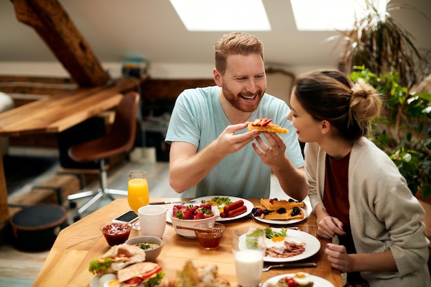 Casal feliz se divertindo enquanto come waffles no café da manhã na mesa de jantar