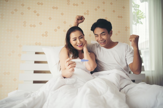 Casal feliz sorrindo depois de descobrir teste de gravidez positivo no quarto