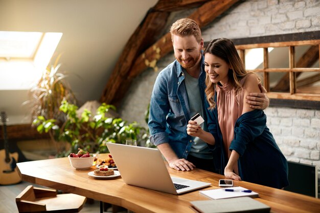 Casal feliz usando laptop e cartão de crédito enquanto faz compras online em casa